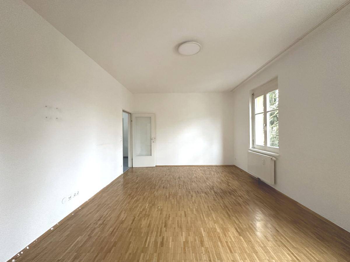 Geräumiges Zimmer mit hellem Parkettboden und einem Fenster, das viel Tageslicht hereinlässt.