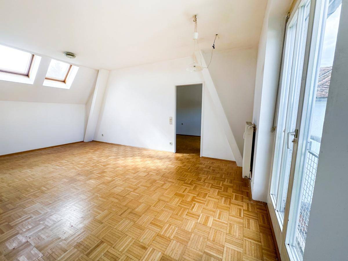 Helles Wohnzimmer mit Parkettboden, Dachschrägen und Zugang zu einem französischen Balkon.