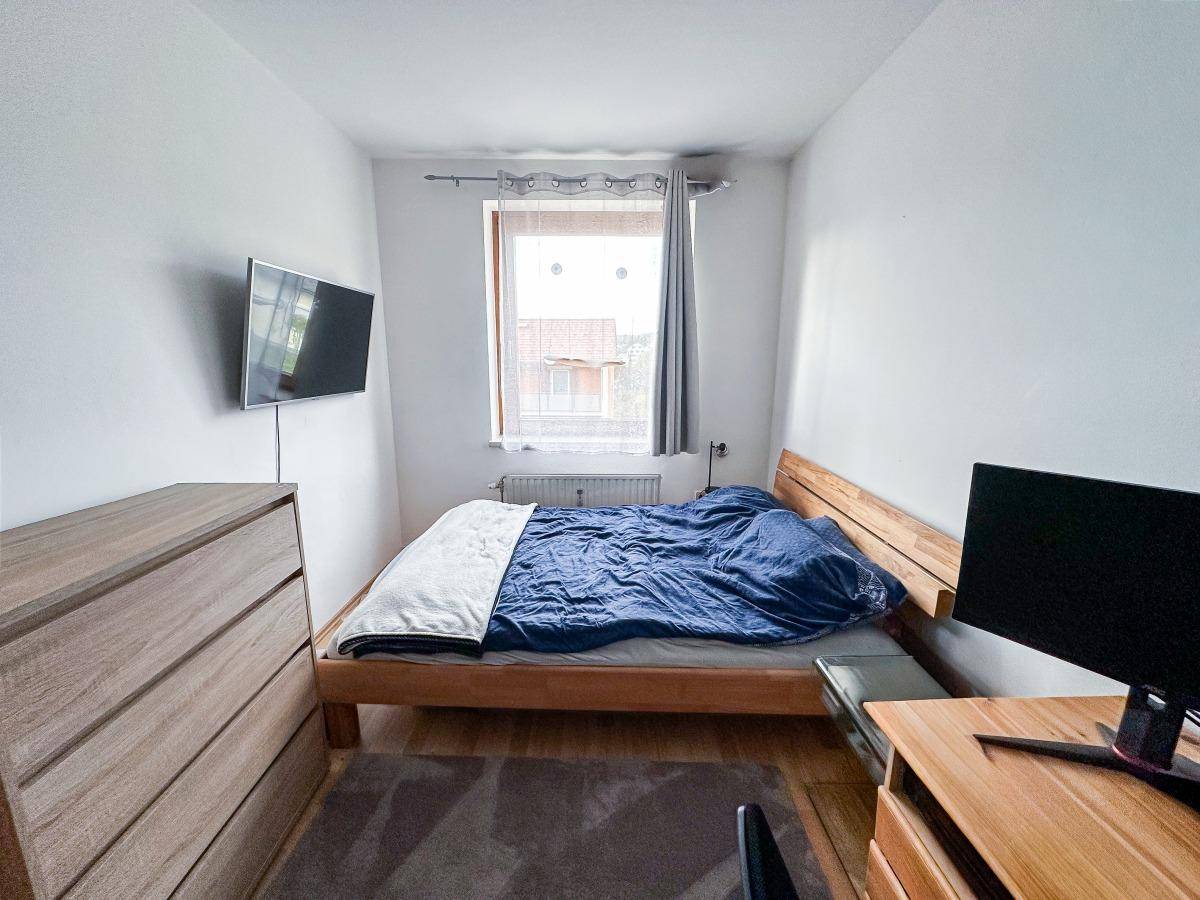 Helles Schlafzimmer mit Holzbett, Kommode und Blick aus dem Fenster.
