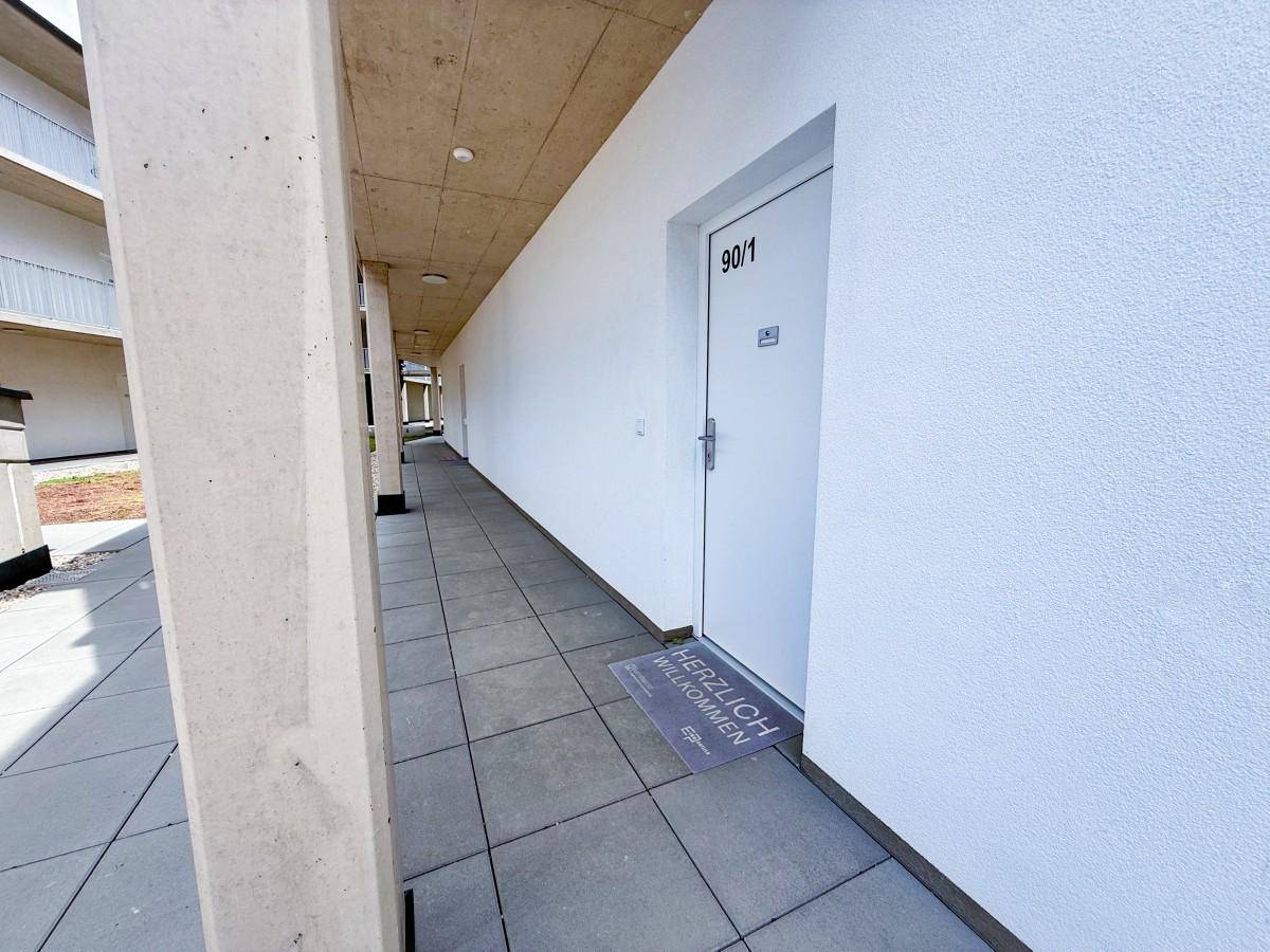 Heller Außenflur mit Fliesenboden, der zu den einzelnen Wohneinheiten des Gebäudes führt.