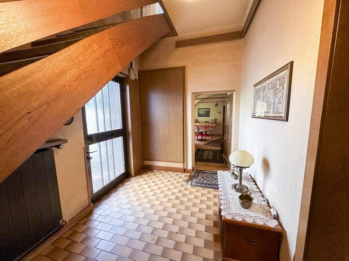 Eingangsbereich mit Holztreppe, Fliesenboden und Zugang zu weiteren Räumen.