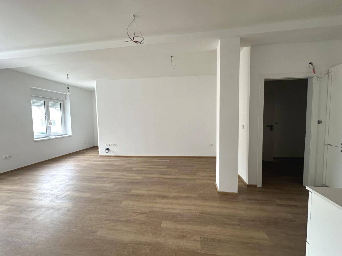 Geräumiges, helles Wohnzimmer mit Laminatboden und weiß gestrichenen Wänden, unmöbliert.