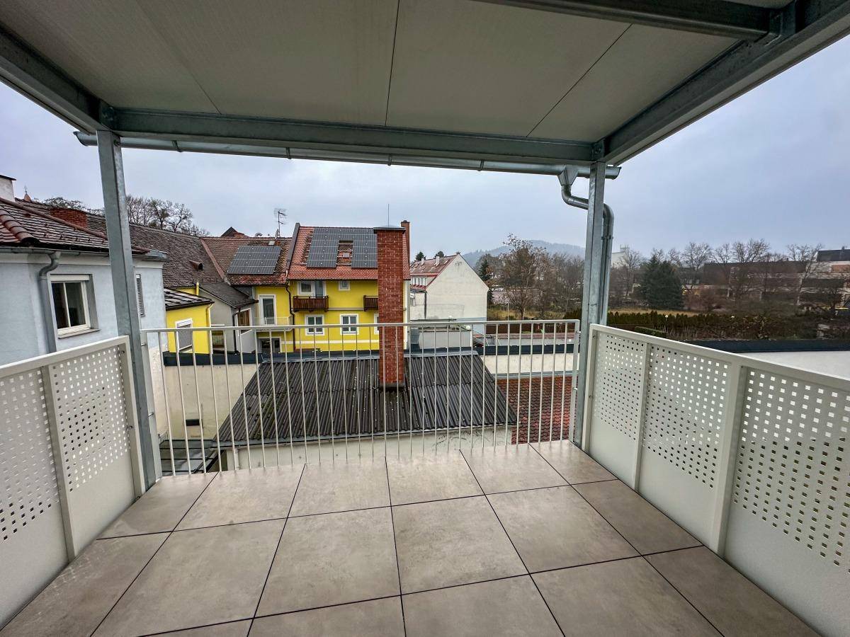 Überdachter Balkon mit Fliesenboden und Blick auf die umliegenden Gebäude und Landschaft.