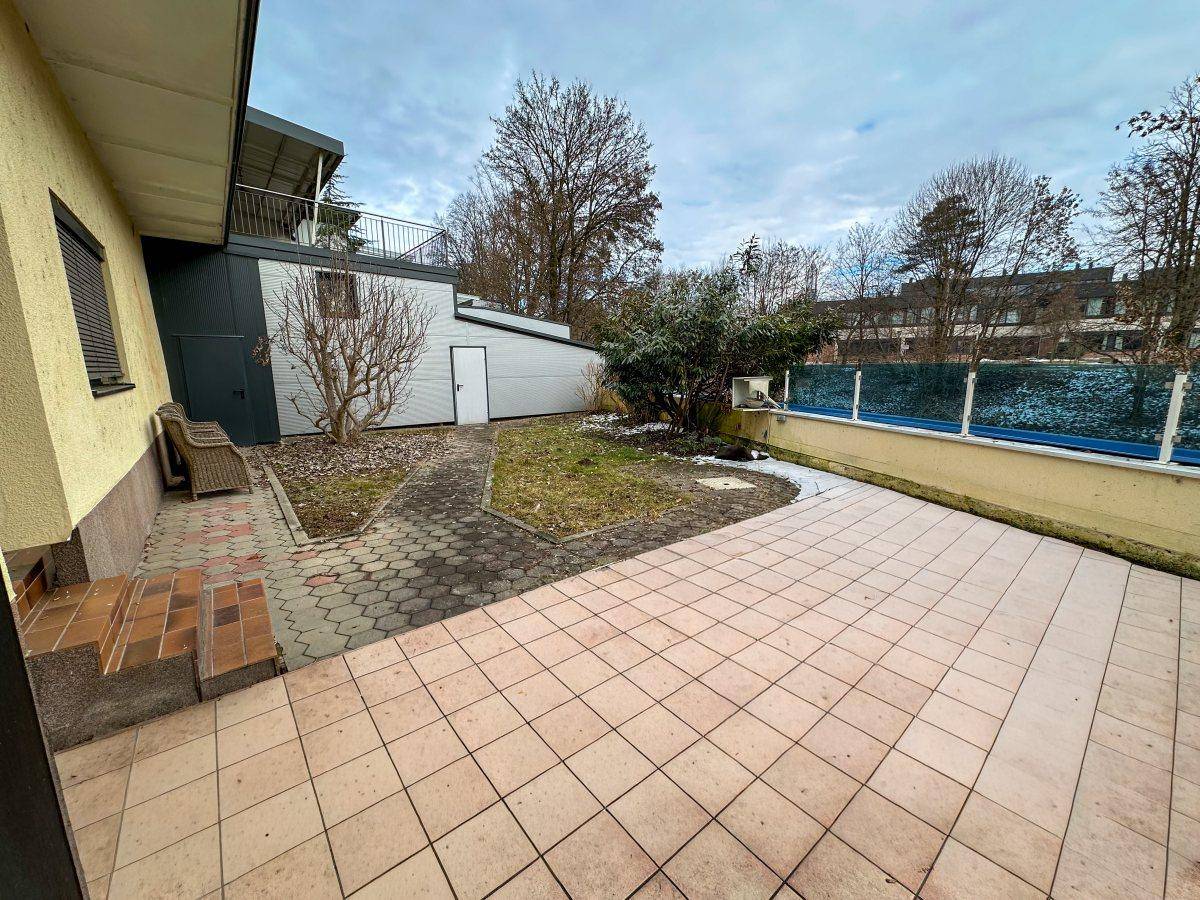 Große geflieste Terrasse mit Sitzgelegenheiten und Blick auf den Gartenbereich.