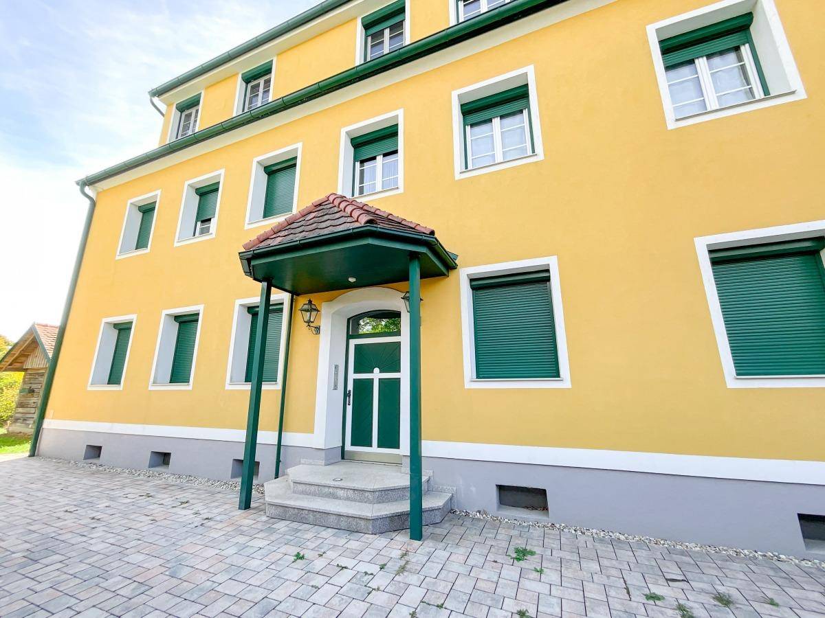 Gelbe Fassade eines Wohnhauses mit grünen Fensterläden und Eingangsbereich.