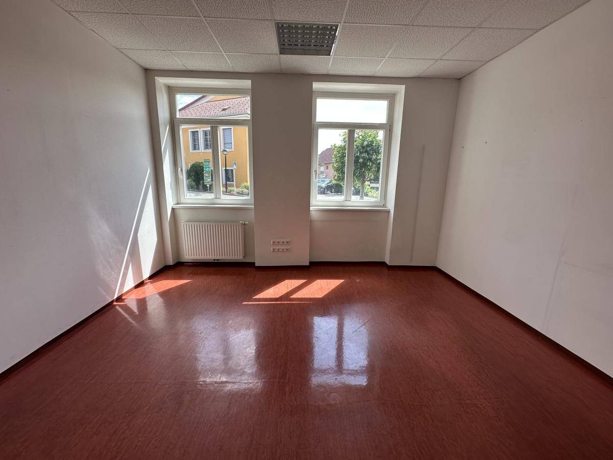 Heller Gewerberaum mit zwei großen Fenstern, braunem Boden und weiß gestrichenen Wänden.