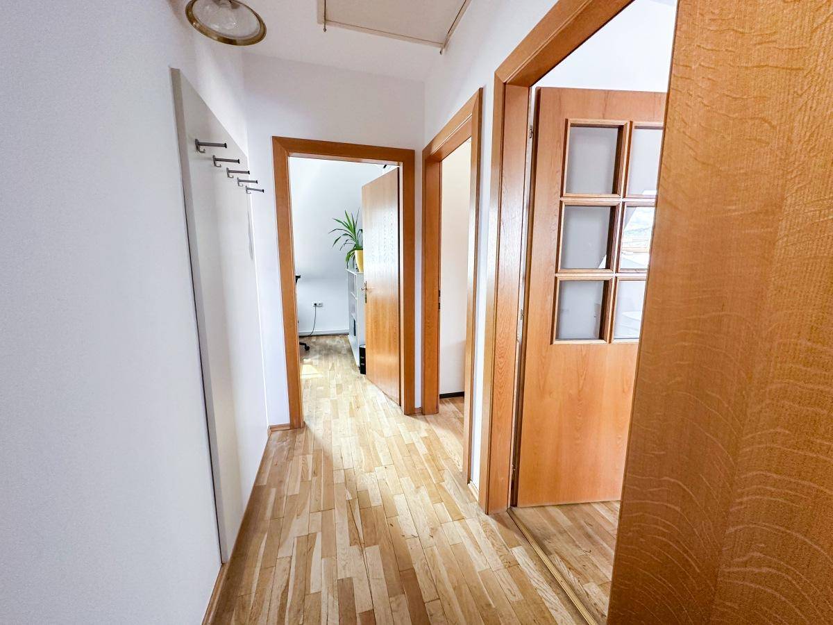 Heller Flur mit Holzfußboden, mehreren Holztüren und einer Garderobe an der Wand.
