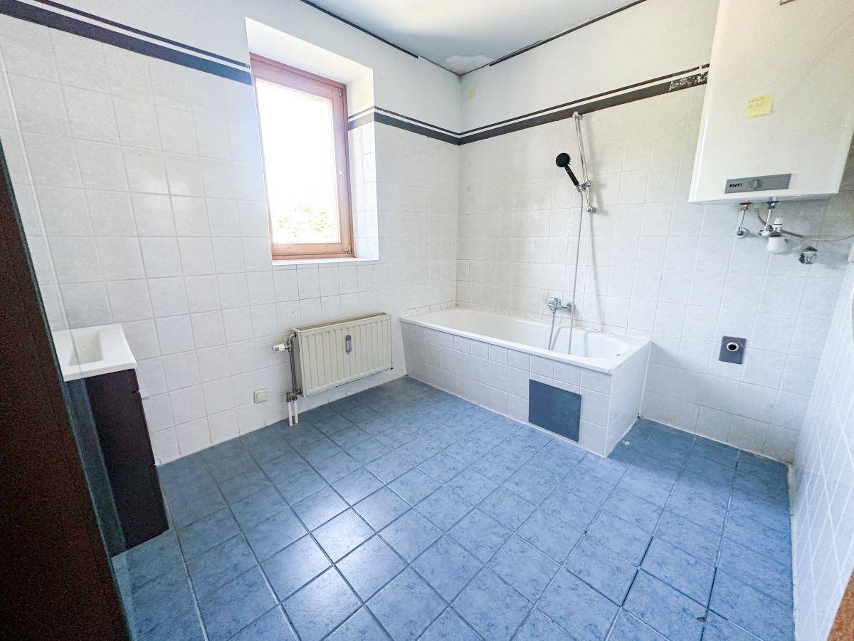 Badezimmer mit blauen Bodenfliesen, weißen Wandfliesen, Badewanne und Fenster für Tageslicht.