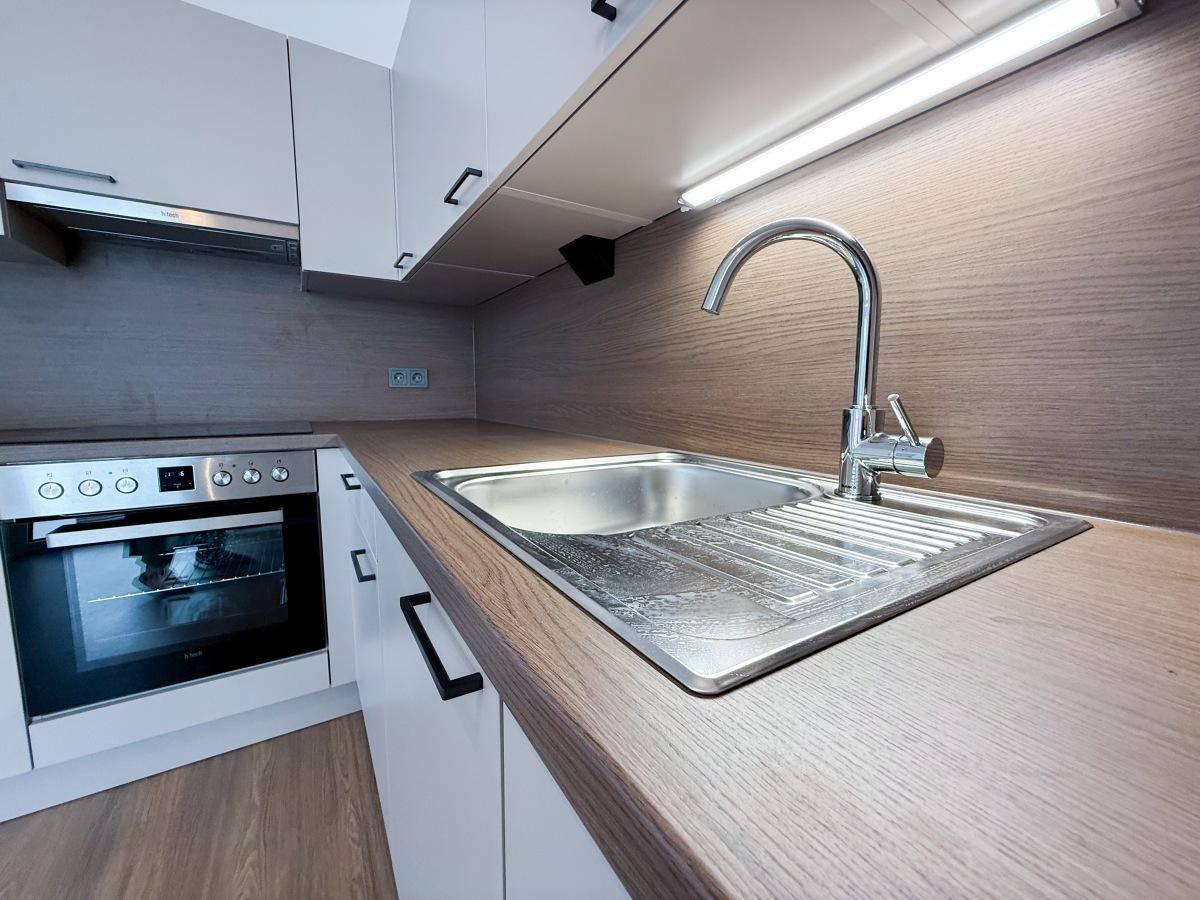 Moderne Küche mit Edelstahlspüle, Holzoptik-Arbeitsplatte und integriertem Backofen.
