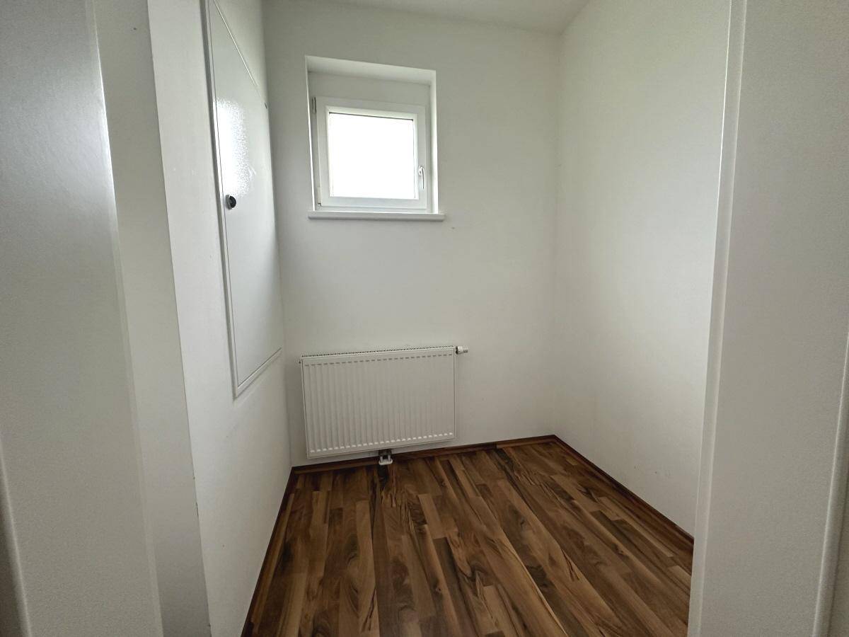Kleiner, heller Raum mit Laminatboden, einem Fenster und Heizkörper, ideal als Büro oder Abstellraum.