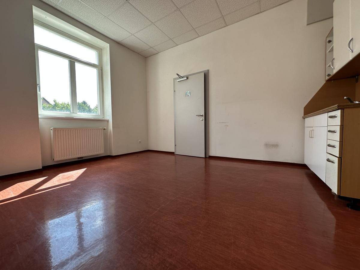 Gewerberaum mit braunem Boden, Fenster und einem kleinen Thekenbereich mit Schränken.