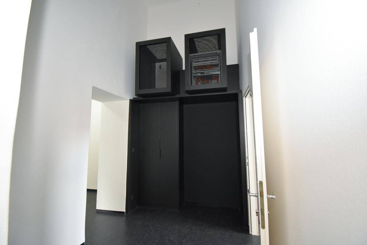 Lagerraum mit schwarzen Schränken und zwei Serverracks an der Decke, bietet viel Stauraum.