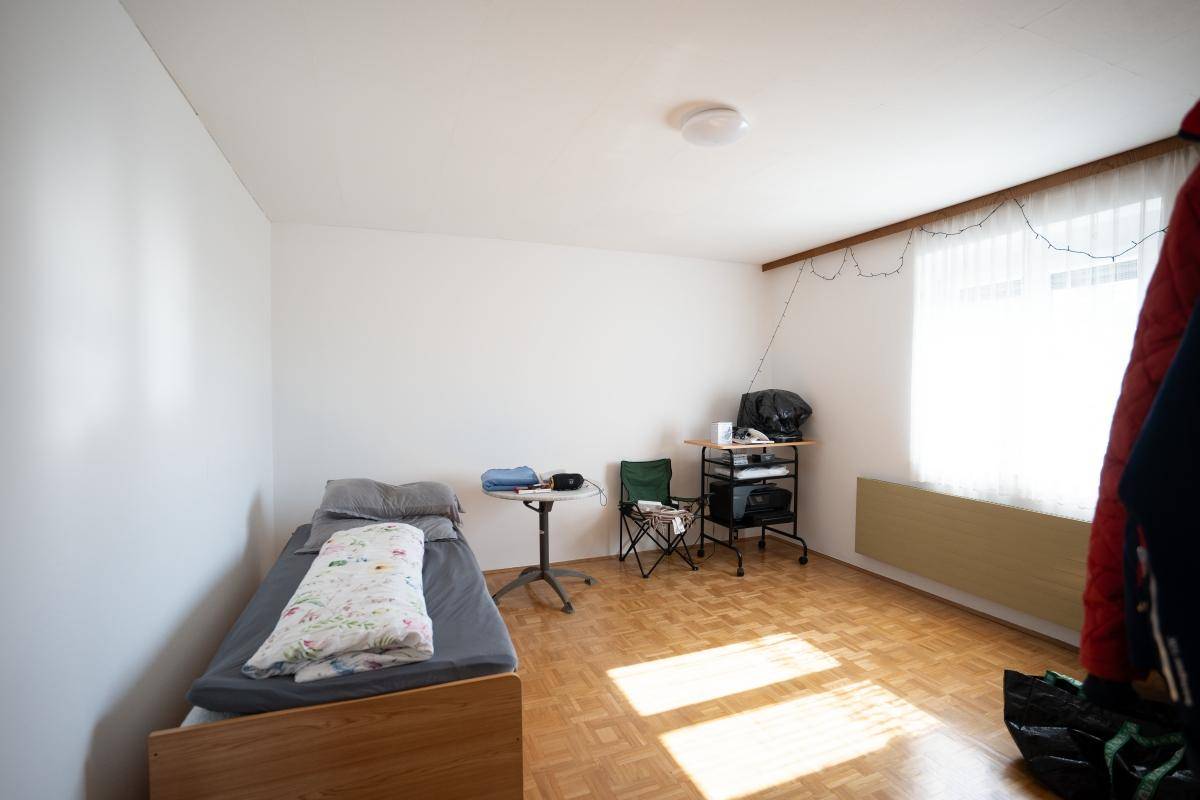 Einfaches Schlafzimmer mit Einzelbett, Holzparkett und Fenster für natürliches Licht.