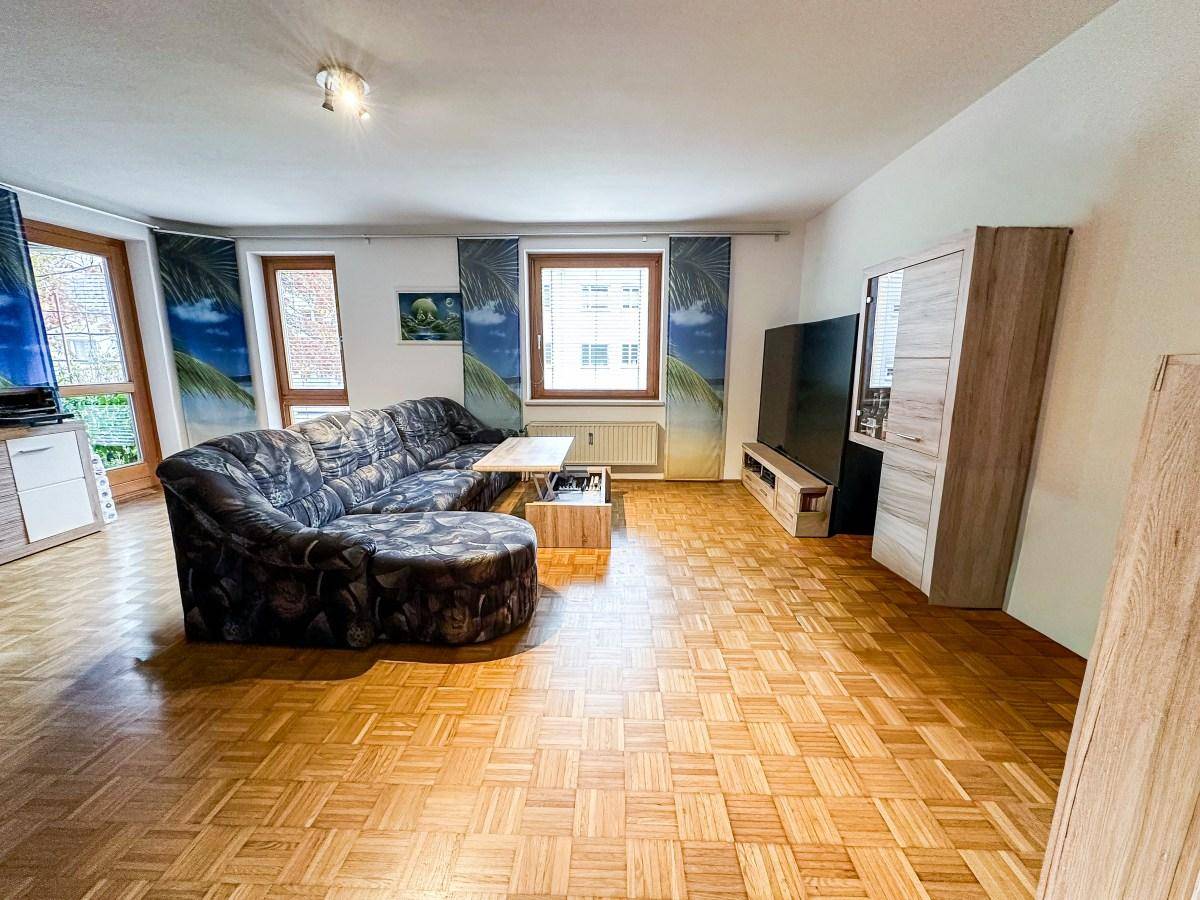 Geräumiges Wohnzimmer mit Parkettboden, großer Eckcouch und viel Tageslicht.