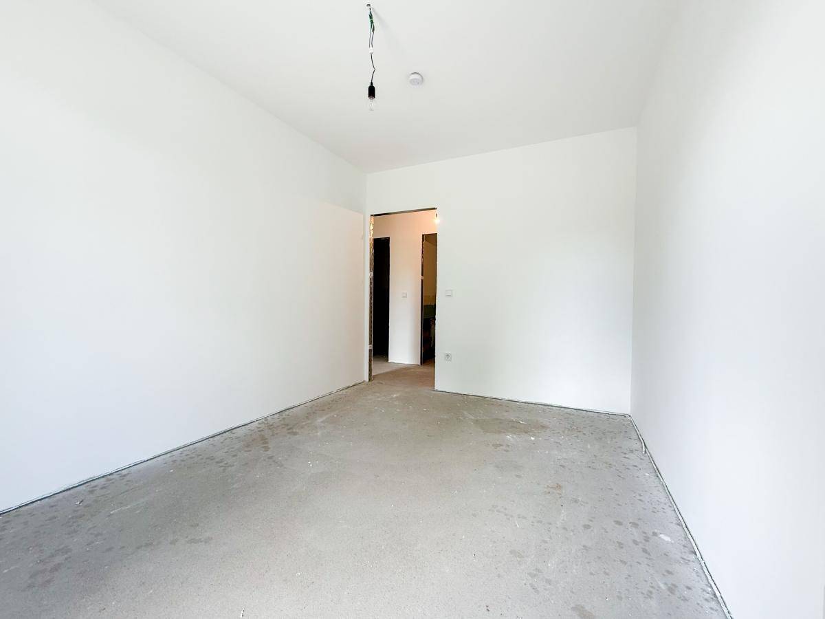 Unfertiger Raum mit weißen Wänden und Betonboden, bereit für den Ausbau und die individuelle Gestaltung.
