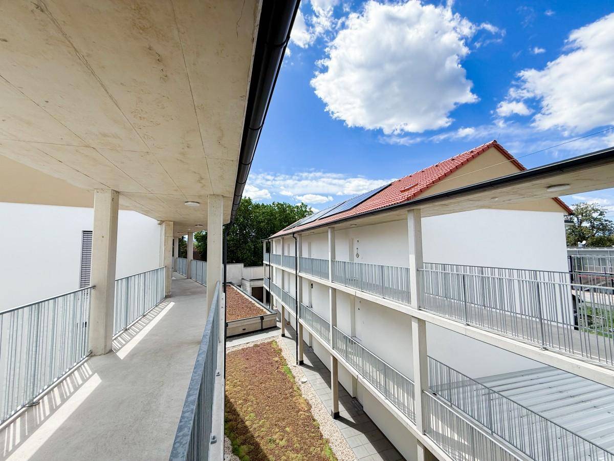 Neubau mit Laubengängen, begrüntem Dach und moderner Architektur in sonniger Umgebung.