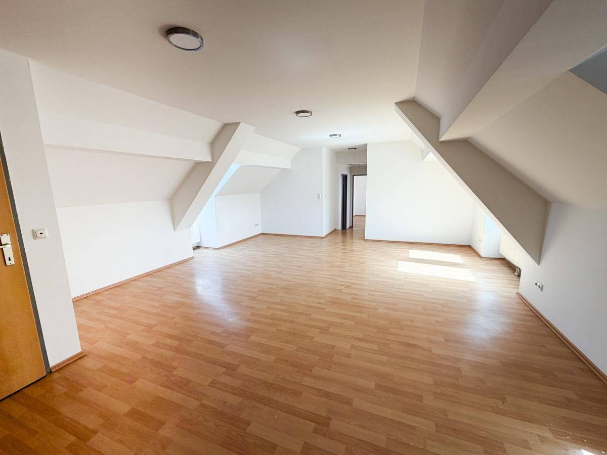 Geräumiger, leerer Wohnbereich im Dachgeschoss mit hellem Laminatboden und charakteristischen Dachschrägen.