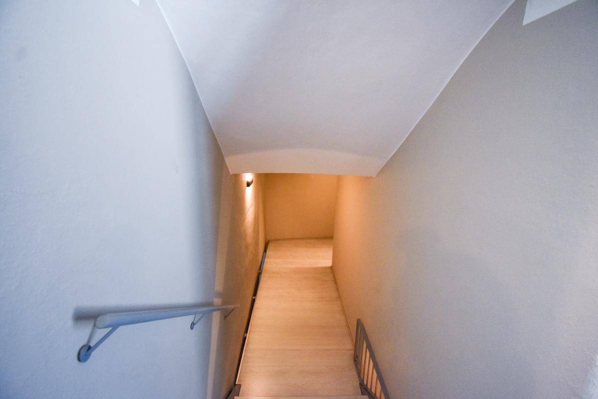 Schlichtes Treppenhaus mit hellem Anstrich und einfachem Handlauf, der nach unten führt.