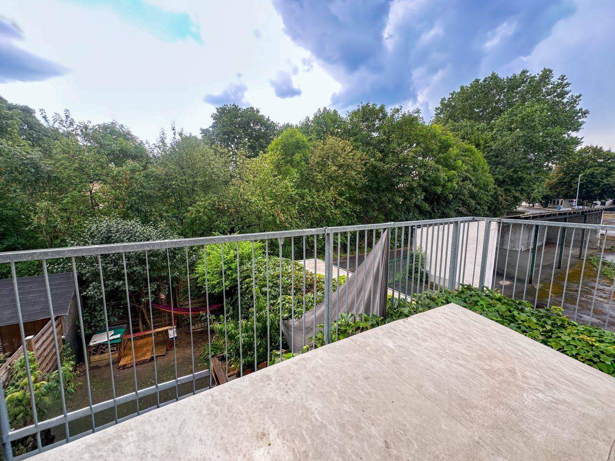 Balkon mit Metallgeländer und weitem Blick über grüne Bäume und die Umgebung.