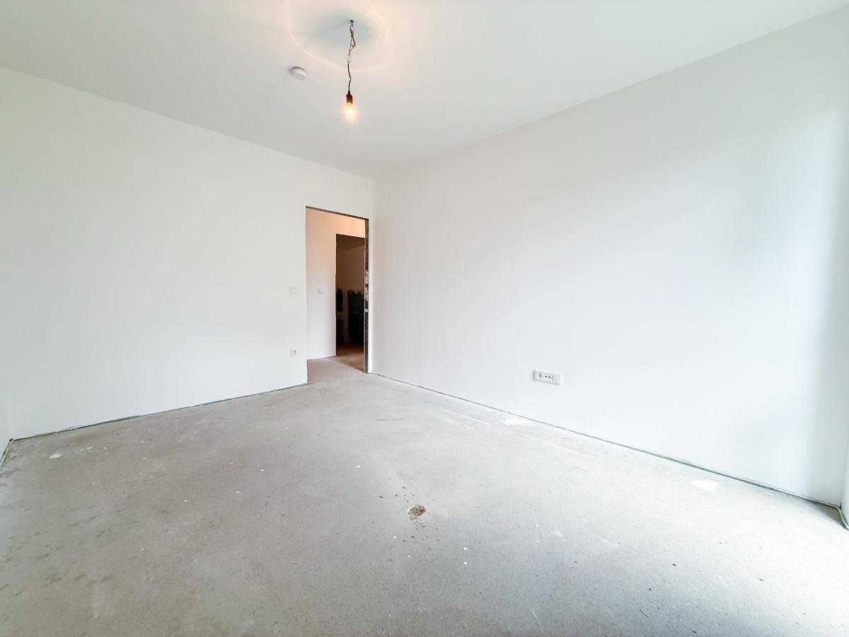 Helles Zimmer im Rohbau mit weiß gestrichenen Wänden und Blick auf den Flur.