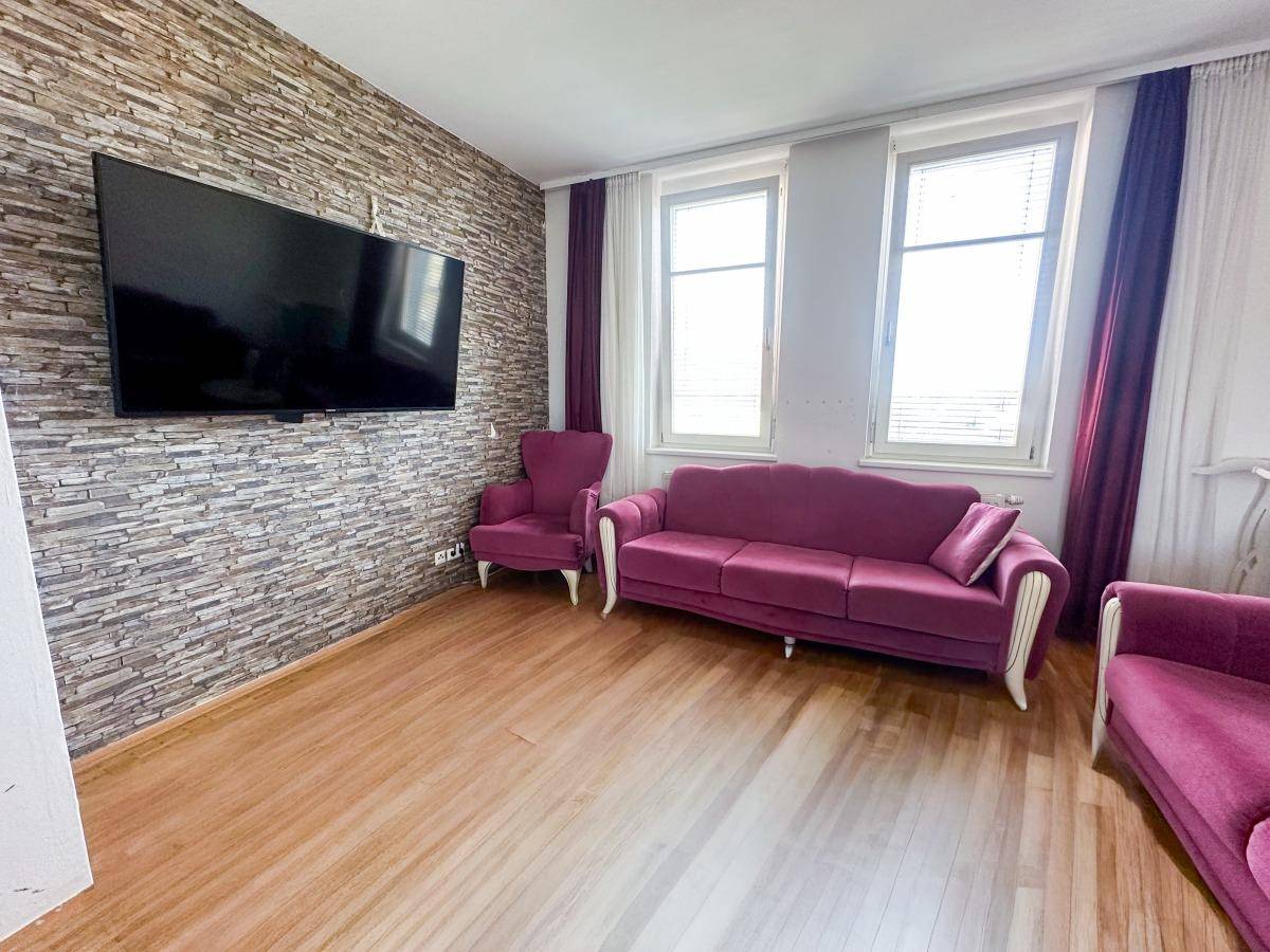 Gemütliches Wohnzimmer mit Steinwand, lila Sofas und großem Wandfernseher.