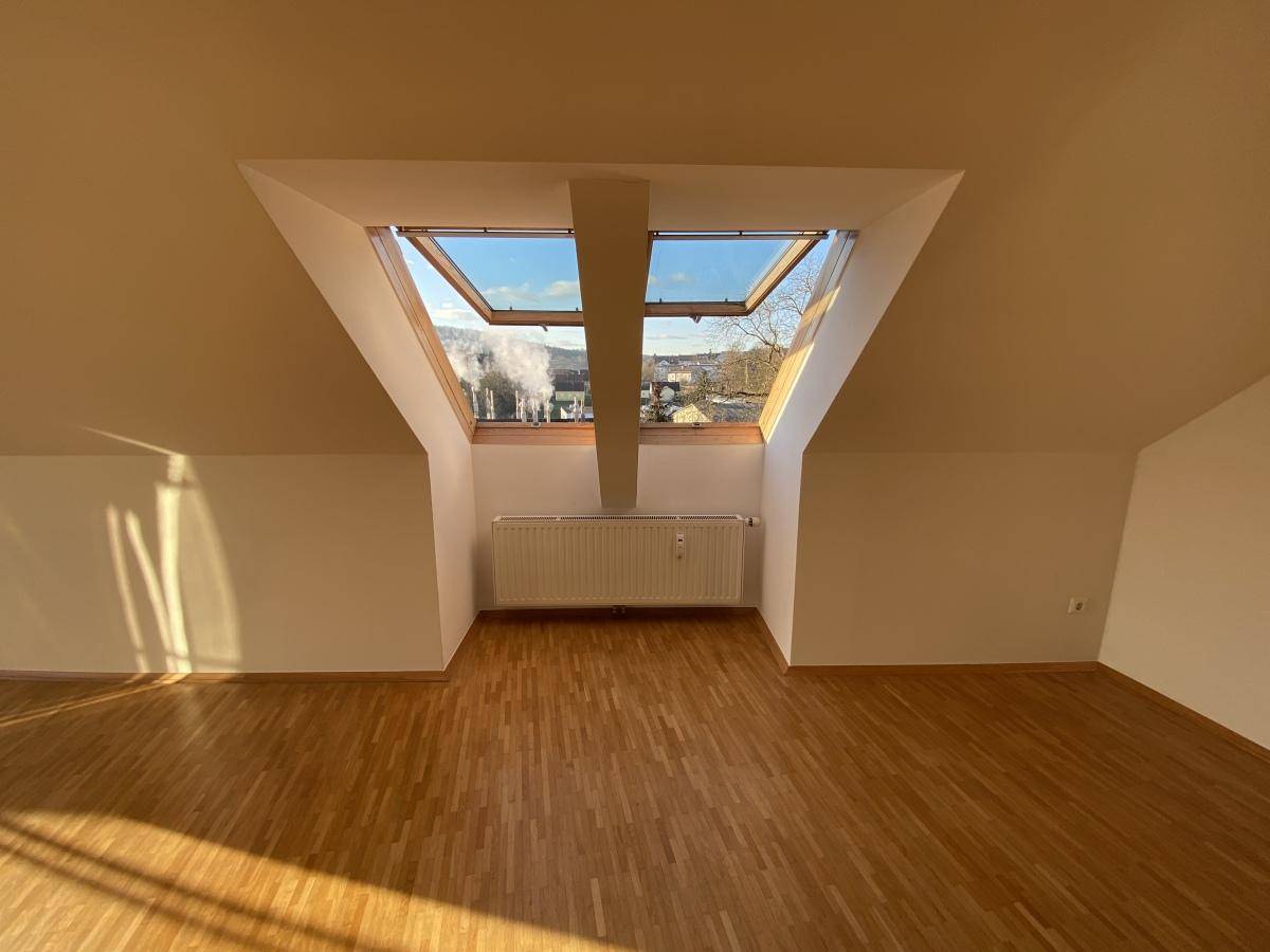 Helles Zimmer im Dachgeschoss mit Holzboden und zwei großen Dachfenstern, die viel Licht hereinlassen.