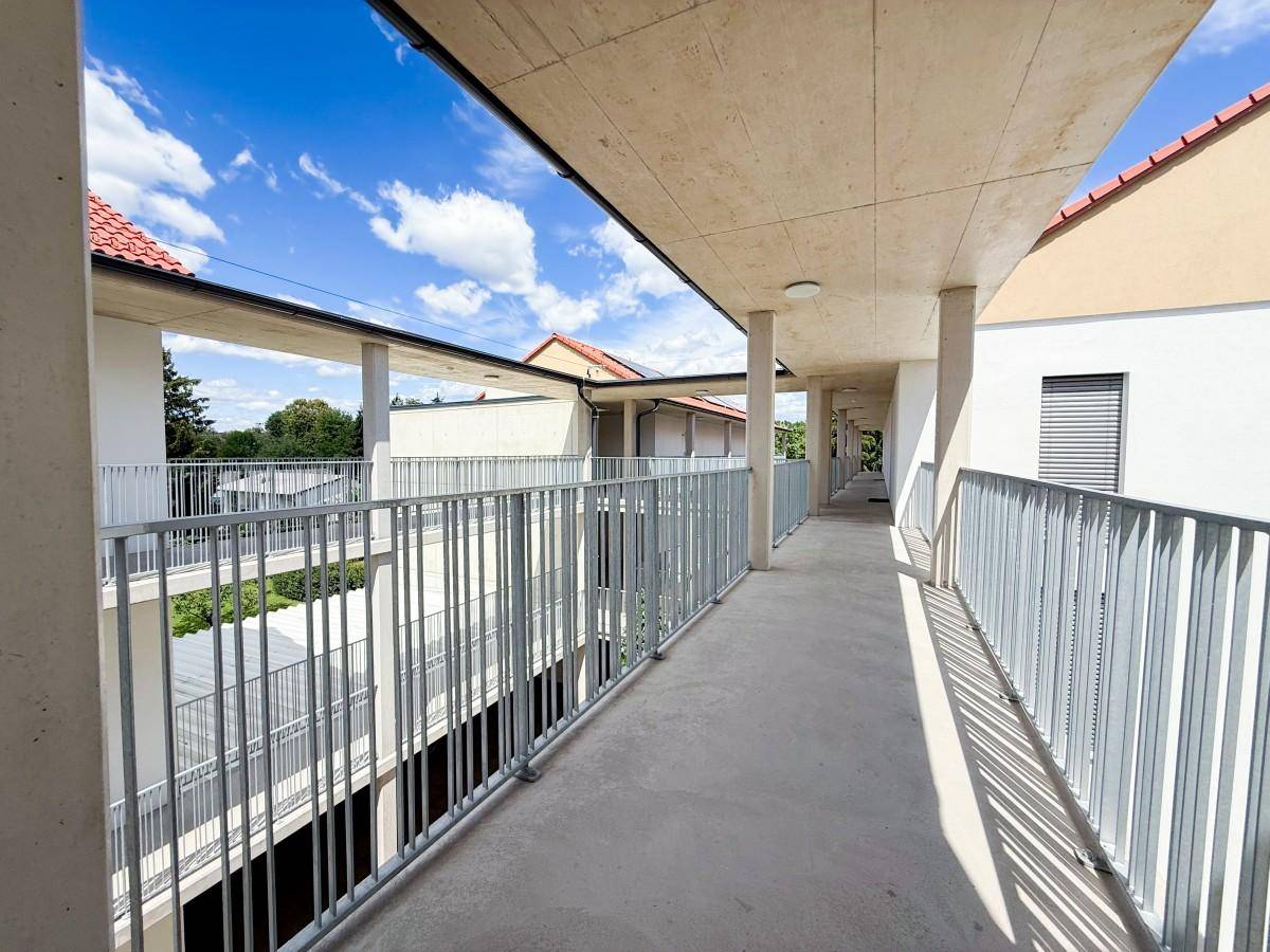 Langer Laubengang eines modernen Apartmentgebäudes mit Blick in den Innenhof.