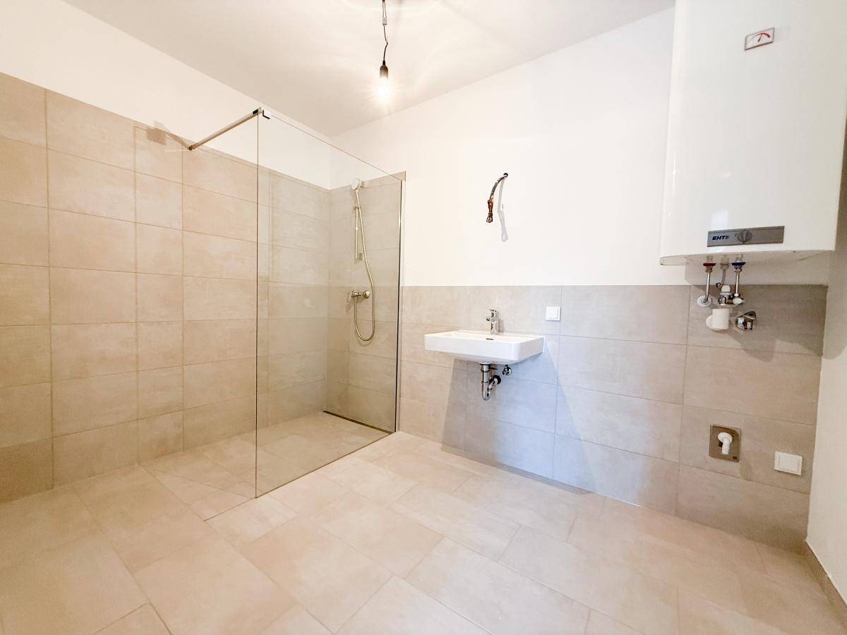 Modernes Badezimmer mit ebenerdiger Dusche, Fliesenboden und Waschbecken.