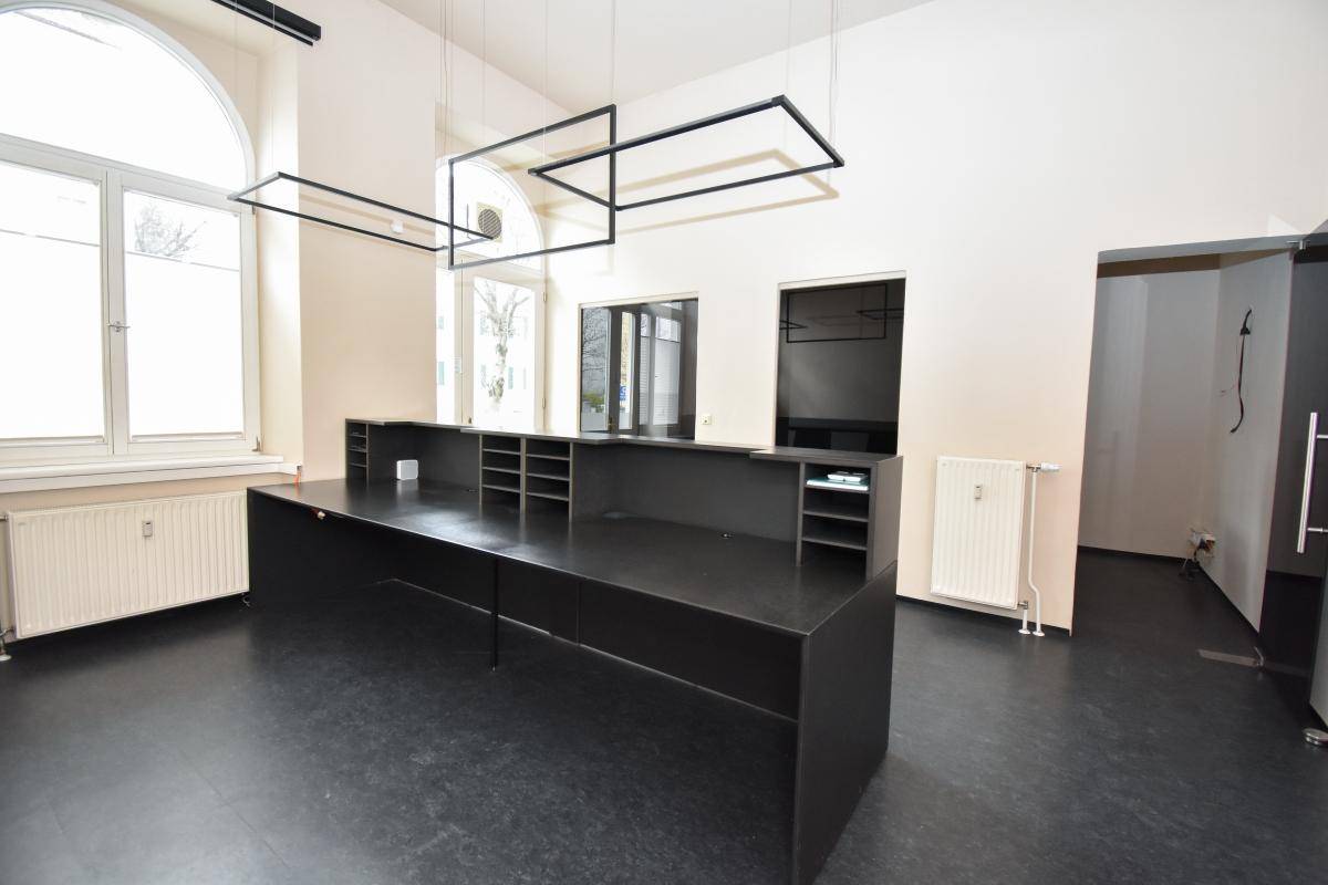 Heller Büroraum mit einer langen schwarzen Theke und modernen Hängelampen, ideal für Empfang oder Arbeitsplätze.