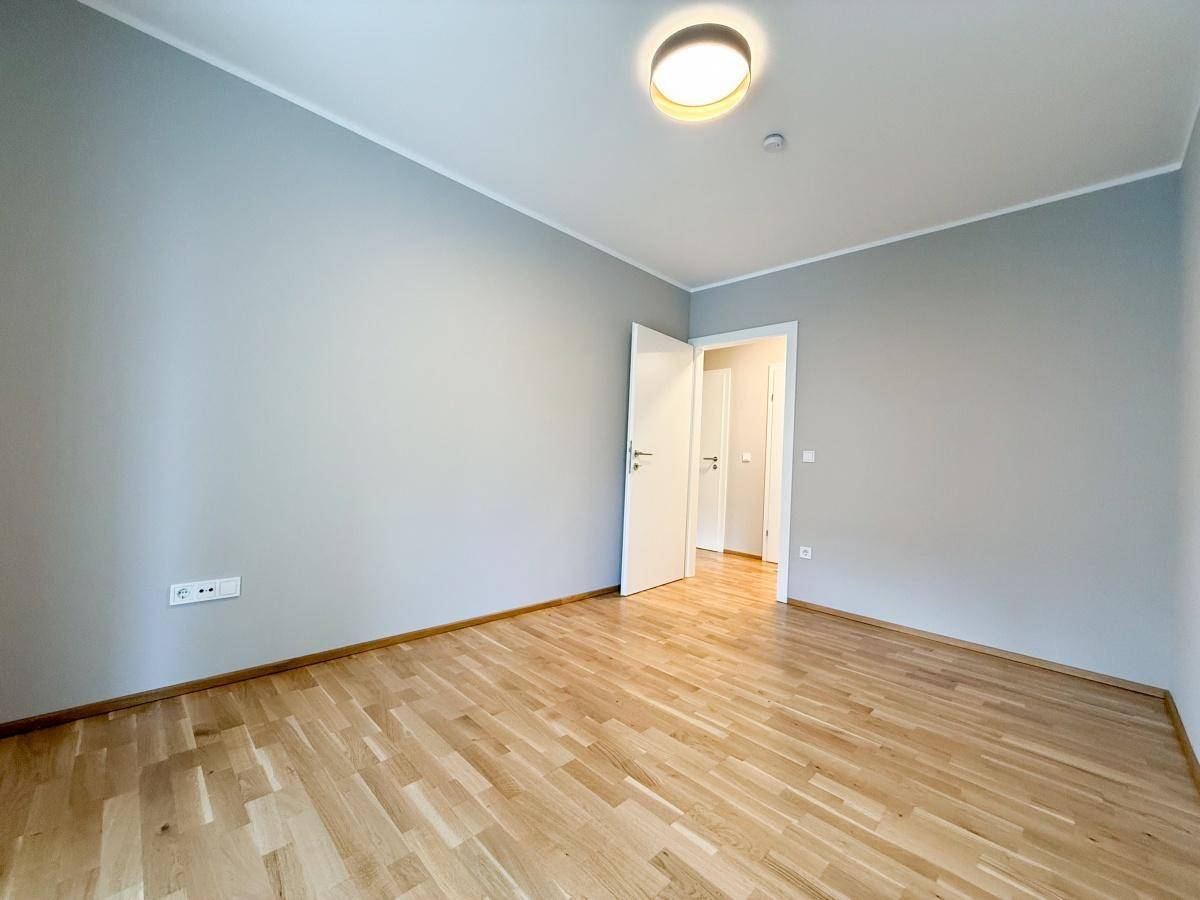 Leerer Raum mit Parkettboden und hellgrauen Wänden.