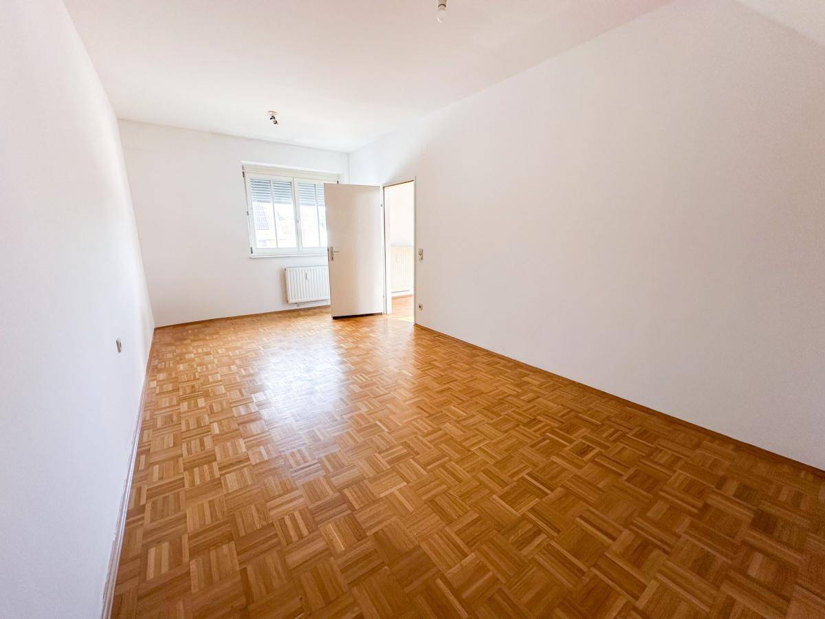 Helles Schlafzimmer mit Parkettboden und einem Fenster mit Rollläden.