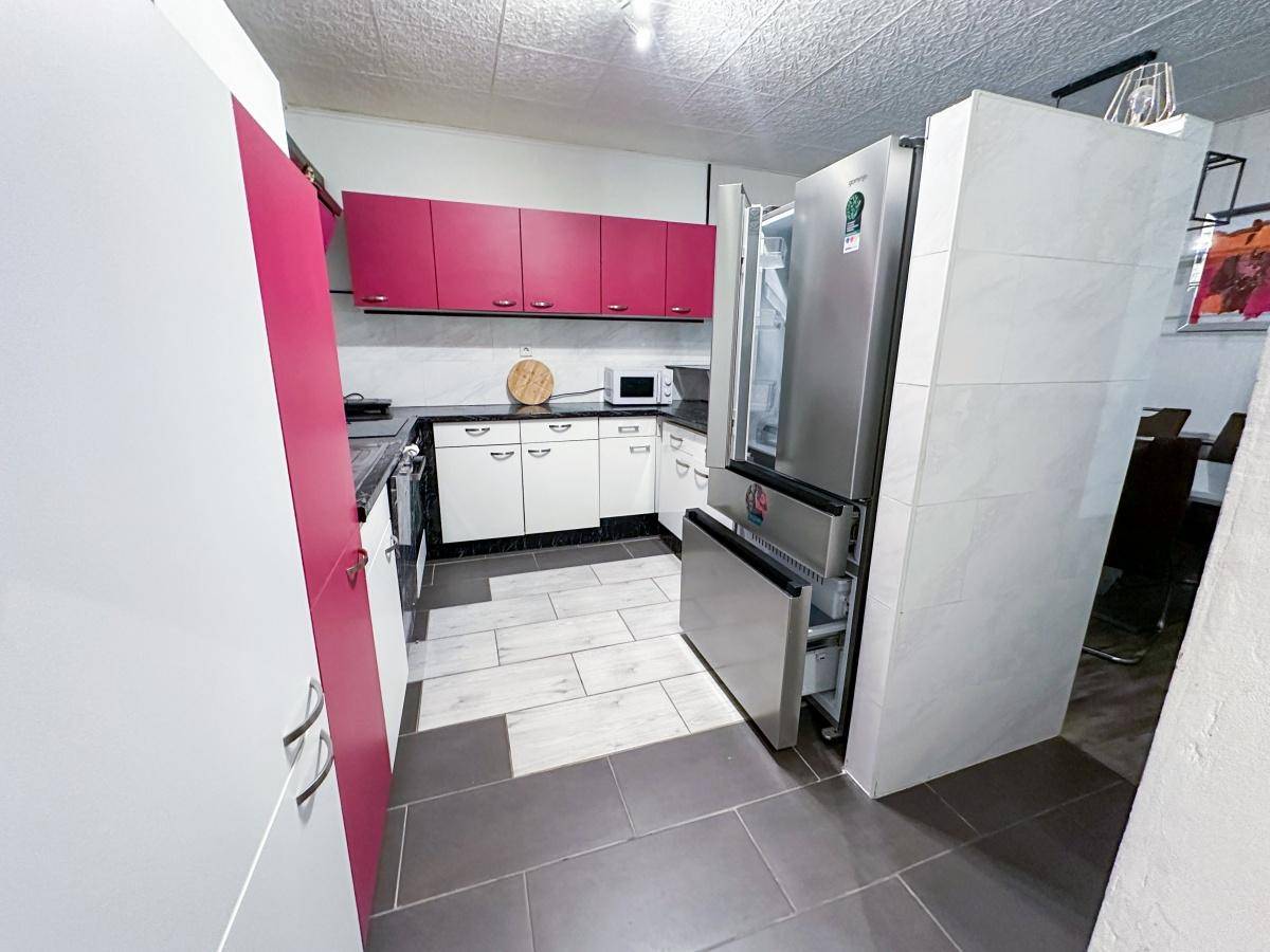 Küche mit weißen und pinken Schränken, modernen Geräten und großem Kühlschrank.