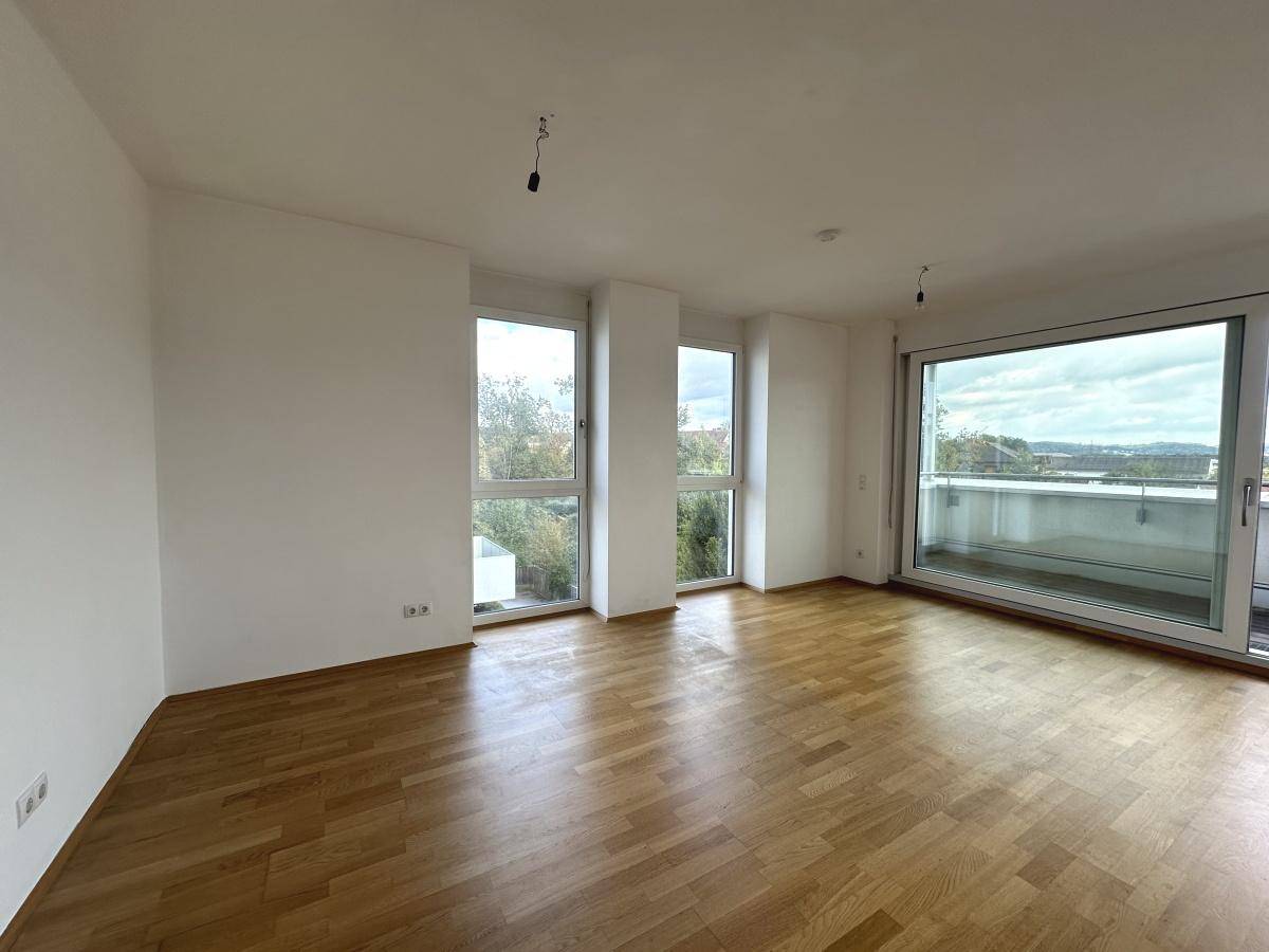 Lichtdurchfluteter Wohnbereich mit Parkettboden, großen Fenstern und Zugang zum Außenbereich.