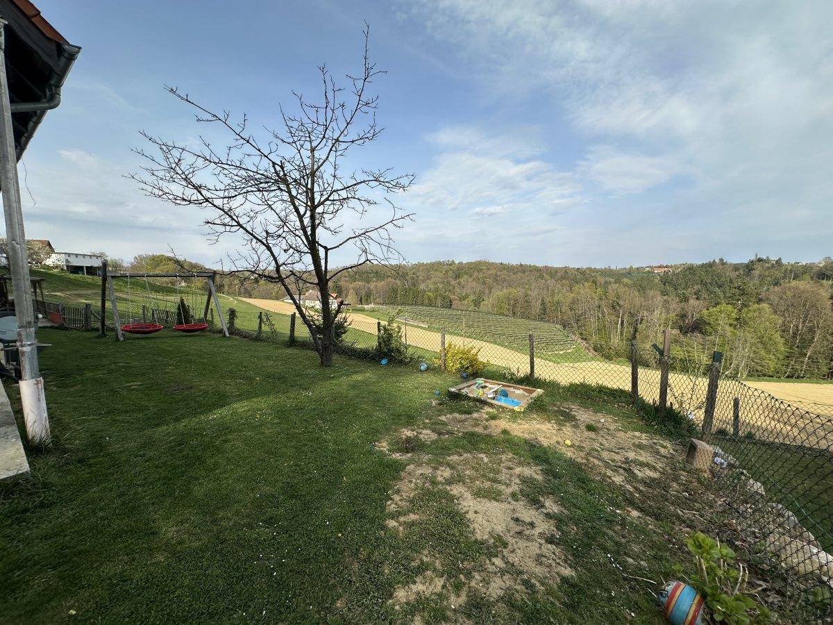 Grüner Gartenbereich mit Schaukeln und Sandkasten, umgeben von Natur und Bäumen.