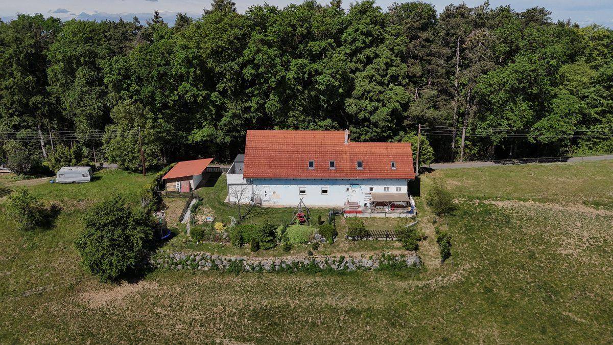 Haus mit rotem Ziegeldach, umgeben von grünen Feldern und Wald, mit kleinem Gartenbereich und Schaukel.