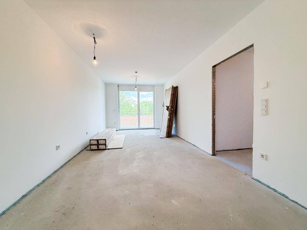 Geräumiger Wohnbereich im Rohbau mit Zugang zu einem Balkon und viel Tageslicht.