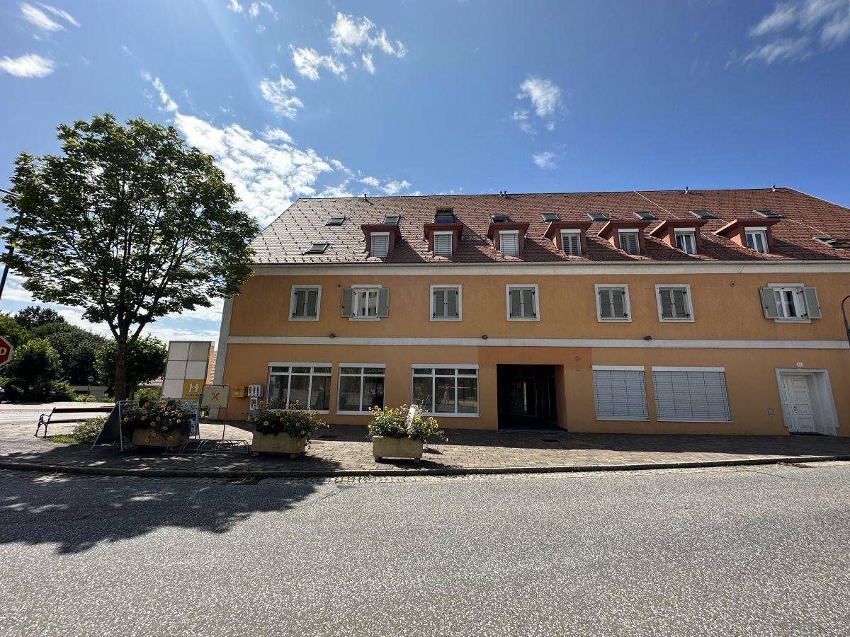 Gesamtansicht des Gebäudes mit orangefarbener Fassade, vielen Fenstern und einem Baum im Vordergrund.