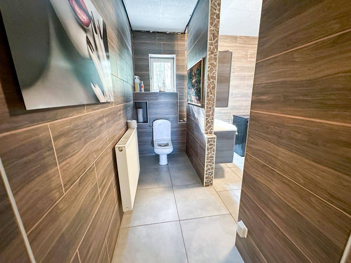Modern gefliestes WC mit dunklen Holzoptik-Fliesen und kleinem Fenster.
