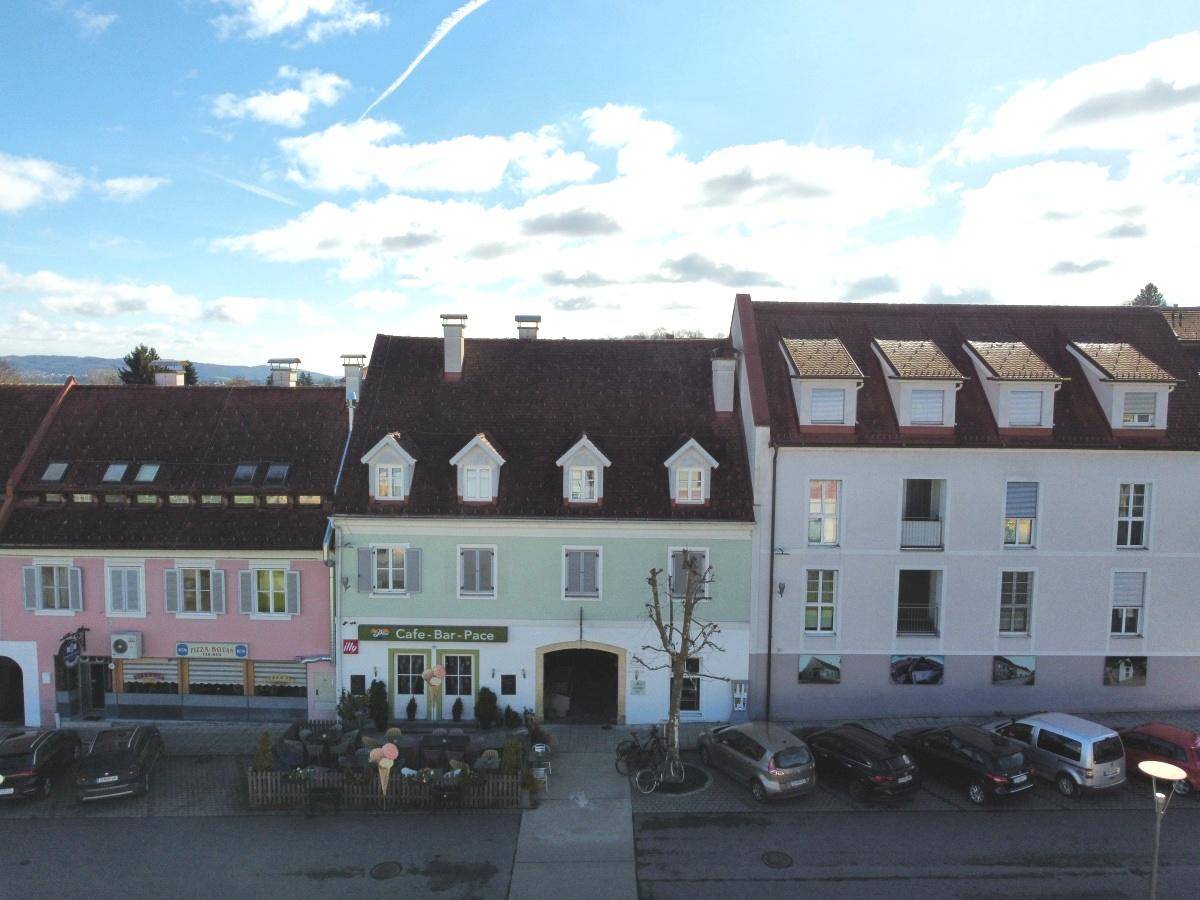 Luftaufnahme des Gebäudes mit Café-Bar im Erdgeschoss und umliegenden Häusern unter blauem Himmel.