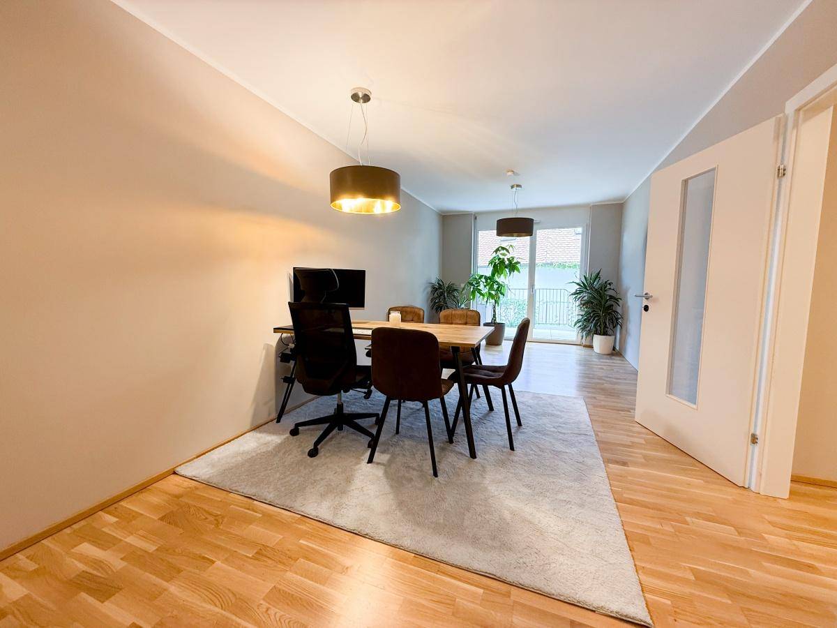 Offener Wohnbereich mit Schreibtisch, Esstisch und Zugang zum Balkon.