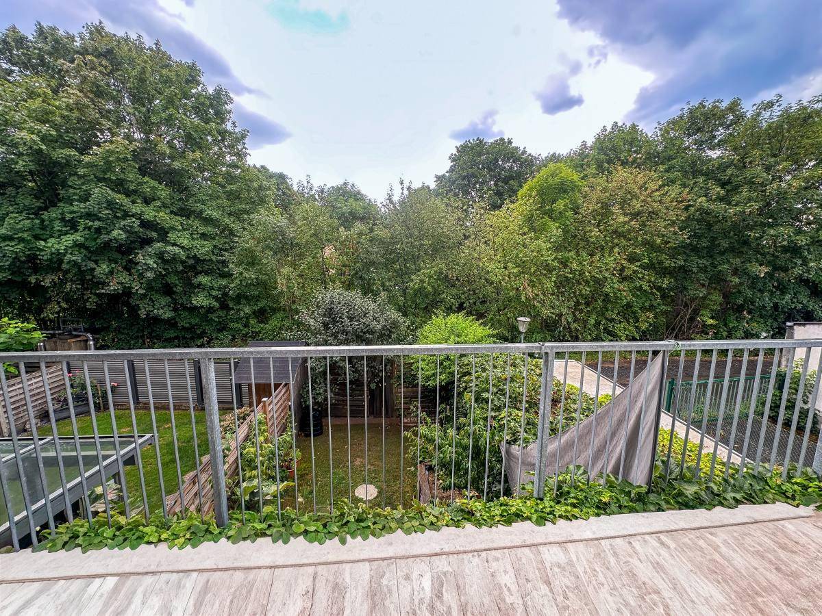 Balkon mit Metallgeländer und Blick auf einen grünen Gartenbereich mit Bäumen.