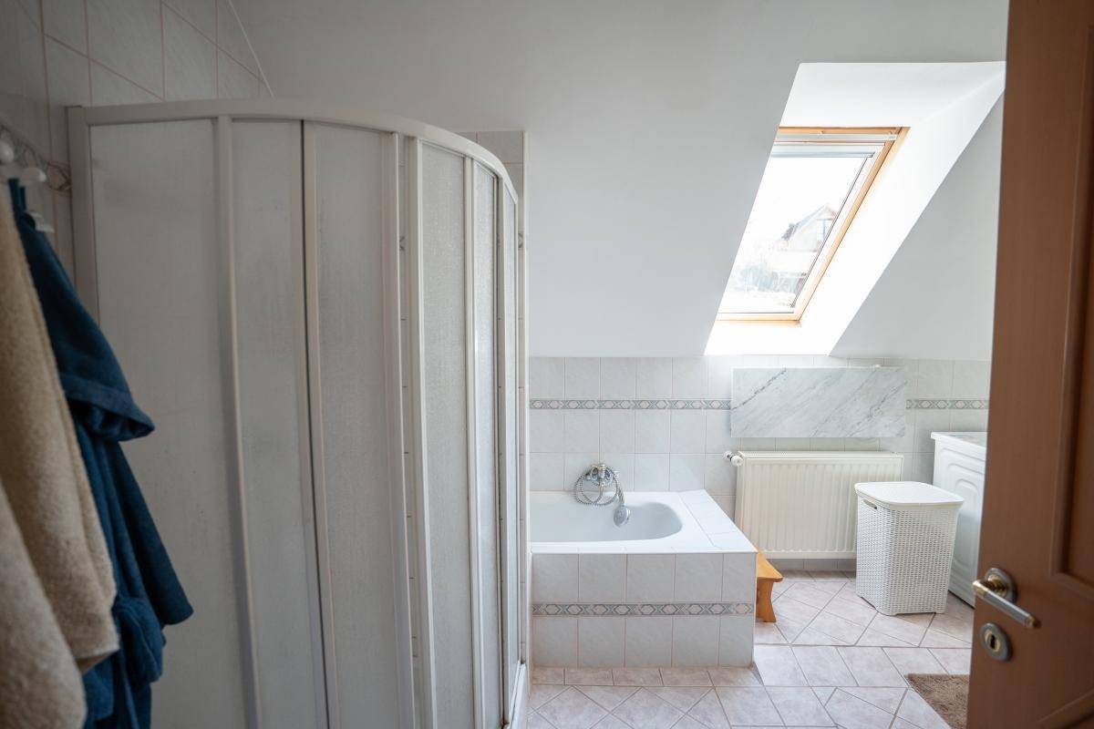 Helles Badezimmer im Dachgeschoss mit Badewanne, Duschkabine und Dachfenster.