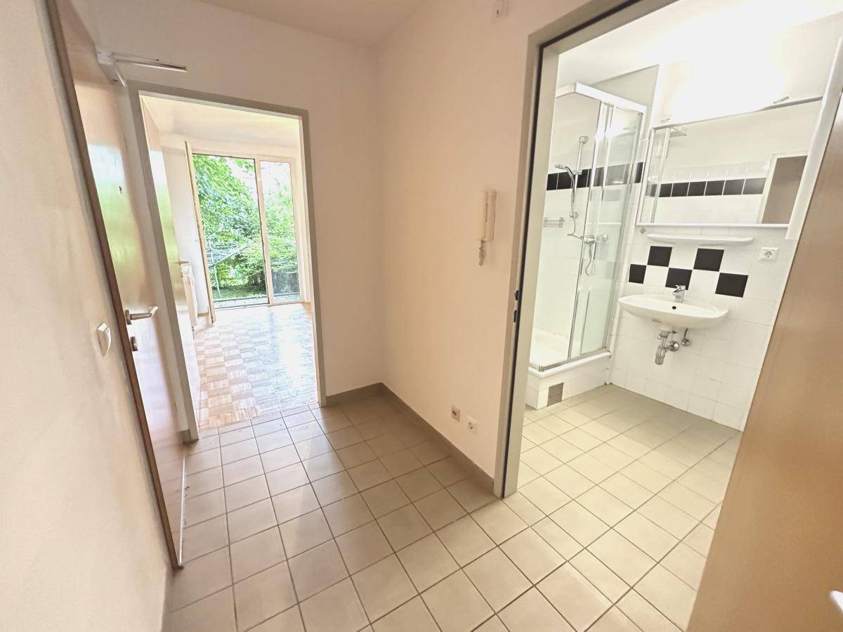 Flur mit Fliesenboden, der zu einem Badezimmer und einem weiteren Zimmer mit Gartenblick führt.