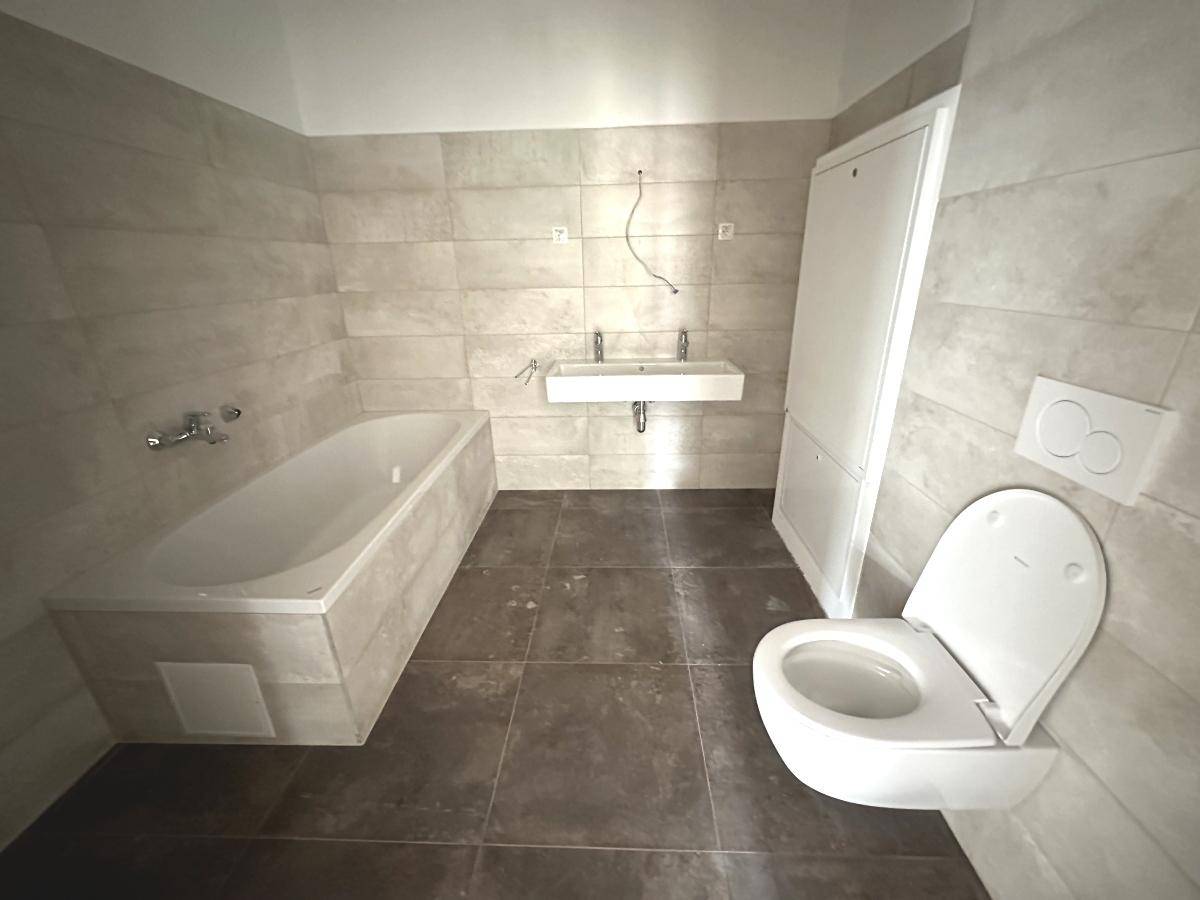 Modernes Badezimmer mit Badewanne, Wand-WC und Doppelwaschbecken, gefliest in hellen Tönen.