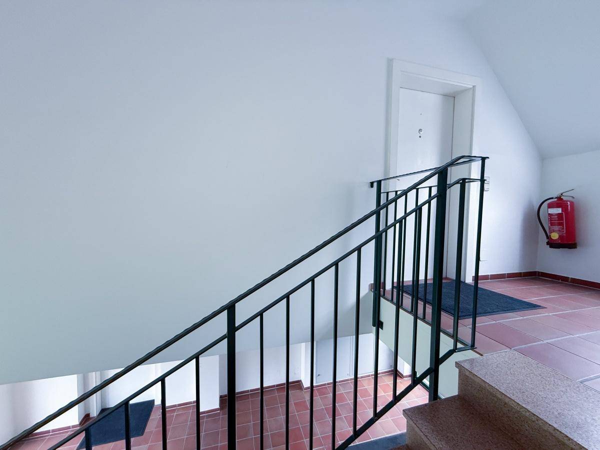 Treppenhaus mit Terrakotta-Fliesen und schwarzem Metallgeländer, inklusive Brandschutzvorrichtung.