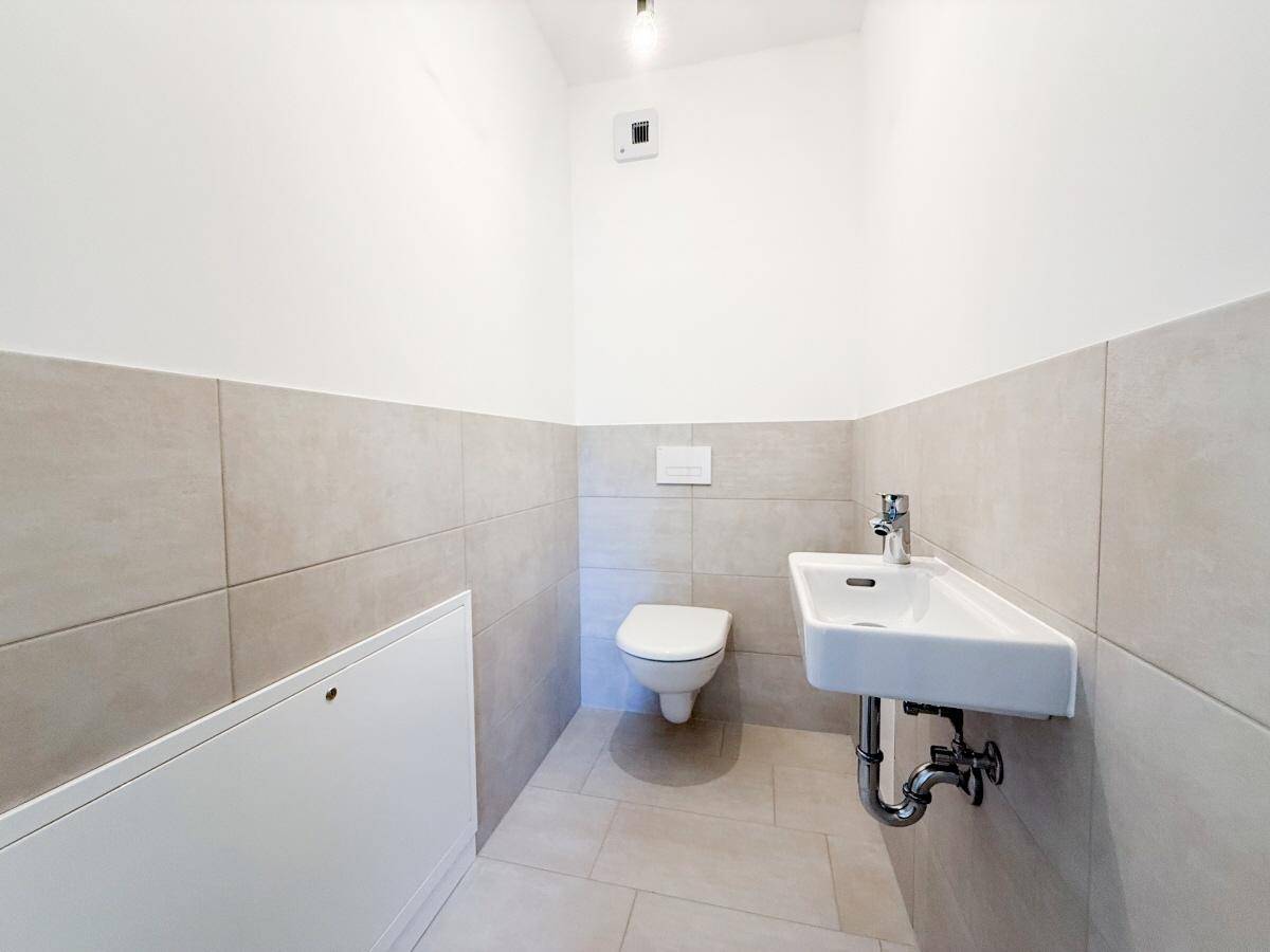 Modernes Gäste-WC mit wandhängender Toilette und kleinem Waschbecken, halbhoch gefliest.