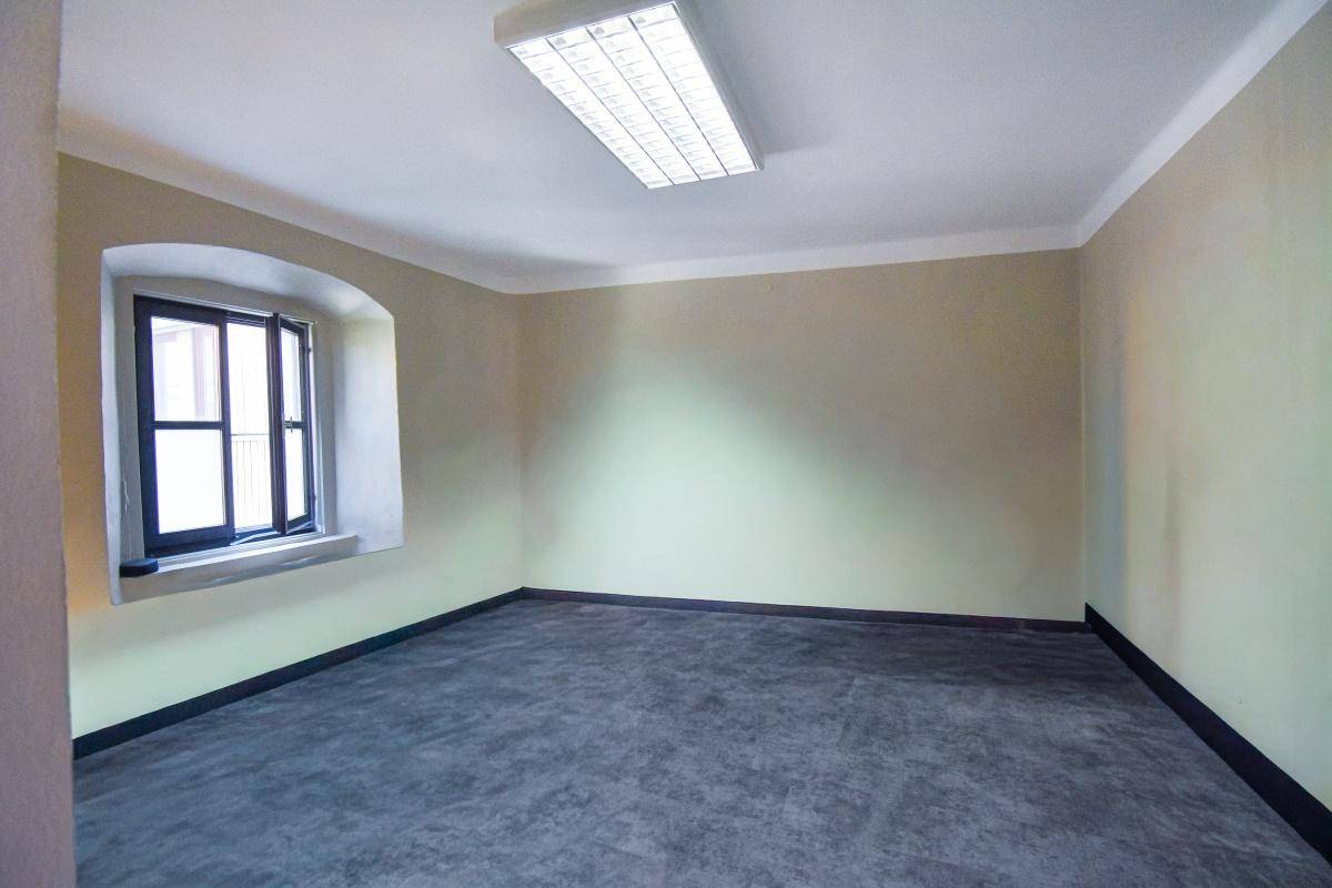 Heller, leerer Raum mit grauem Bodenbelag und einem kleinen Fenster, beleuchtet von einer Deckenleuchte.