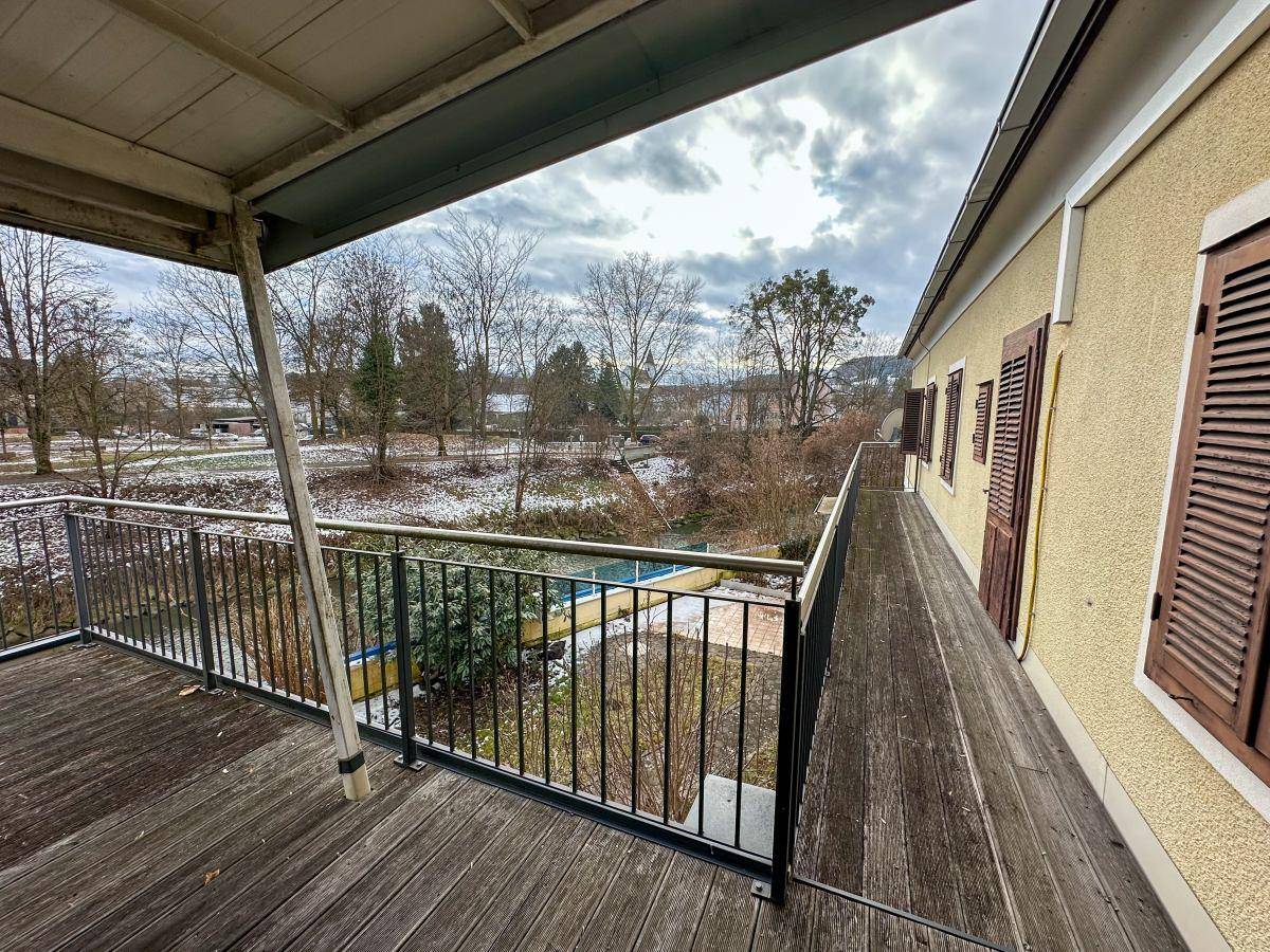 Langer Balkon mit Holzboden und Blick auf den Garten und die Umgebung.