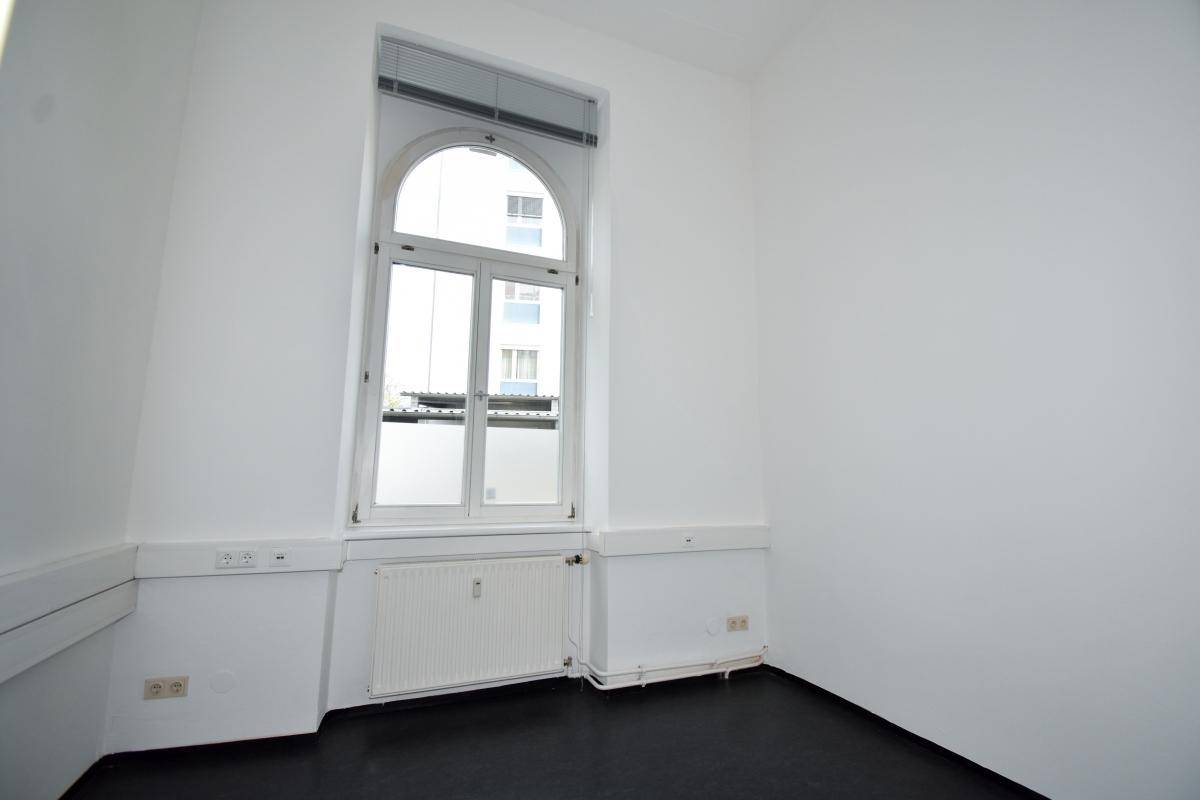 Heller Büroraum mit einem großen Bogenfenster und weißen Wänden, bietet viel Tageslicht.