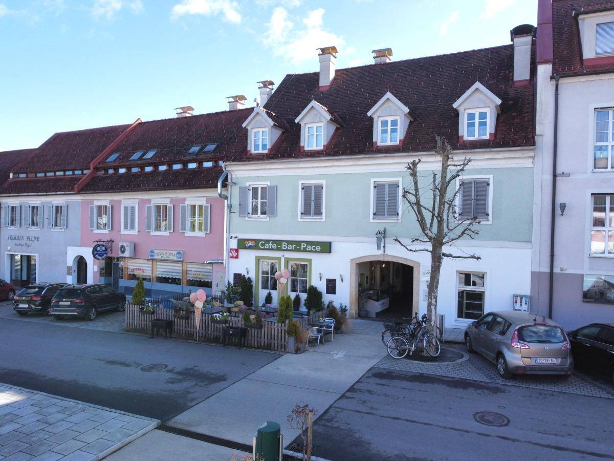 Ansicht des Gebäudes mit Café im Erdgeschoss, Außenbereich und parkenden Autos auf der Straße.